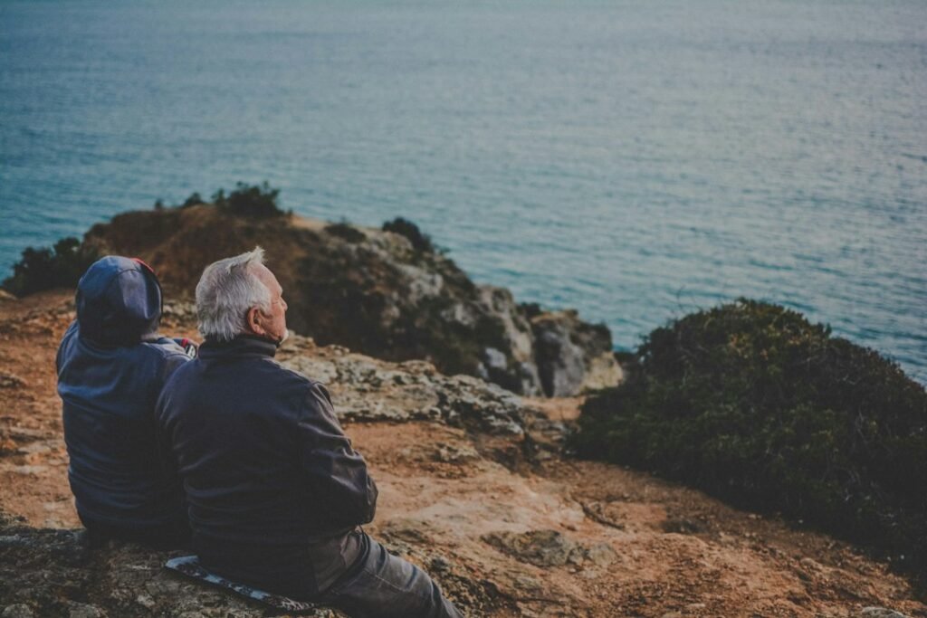 Dos personas contemplando el mar desde una roca, cuenta ahorro-inversión vs plan de pensiones