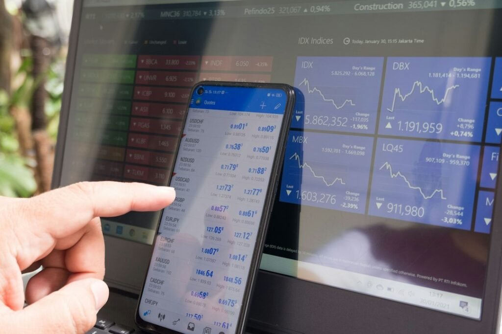 Mano señalando una app de trading en un smartphone junto a un portátil, para elegir el mejor bróker por fiscalidad