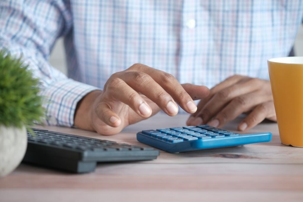 Persona usando una calculadora en el escritorio con una taza de café, comparando declaración conjunta e individual
